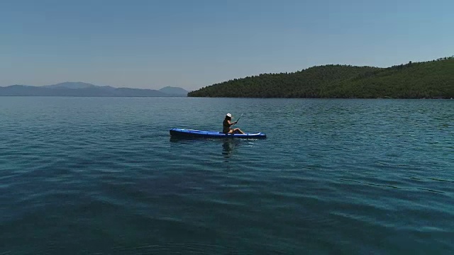 一个孤独的女人在湖上或海上划皮艇。一个快乐的成熟女人在一个夏天的湖中或海里划独木舟。视频素材