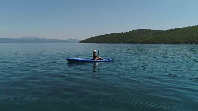 一个孤独的女人在湖上或海上划皮艇。一个快乐的成熟女人在一个夏天的湖中或海里划独木舟。视频素材