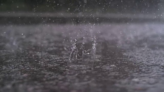 慢镜头特写:雨滴落在街道上，形成一个大水坑视频素材