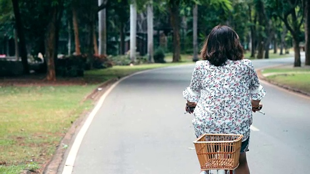 年轻的亚洲女人在公园里骑自行车，慢镜头视频素材