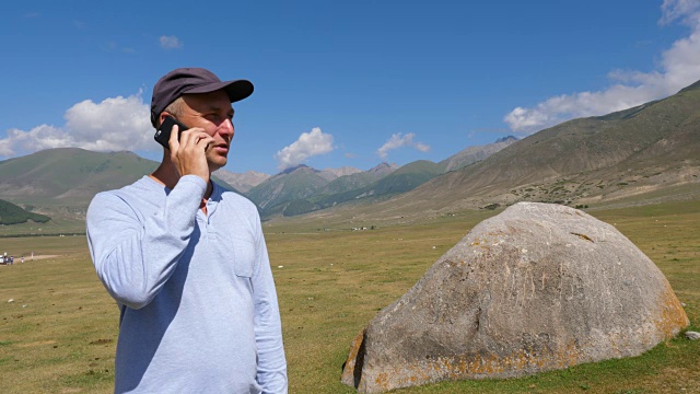 男人打电话给手机，而山上旅行在绿色高地景观视频素材