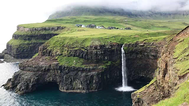 在Vagar岛的Mulafossur瀑布与Gasadalur村的背景，令人惊叹的壮观景观在北大西洋中部的法罗群岛目的地视频素材