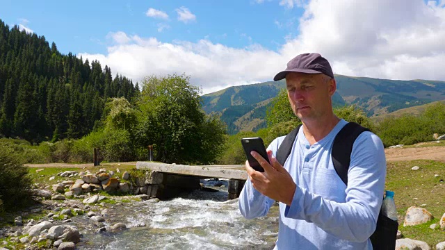 成年男子浏览手机时，在石河景观山徒步旅行视频素材