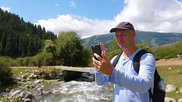 在河流湍急的山区旅行时，一名男子用智能手机进行视频聊天视频素材