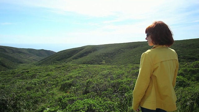 红发女人俯瞰着草山和海景视频素材