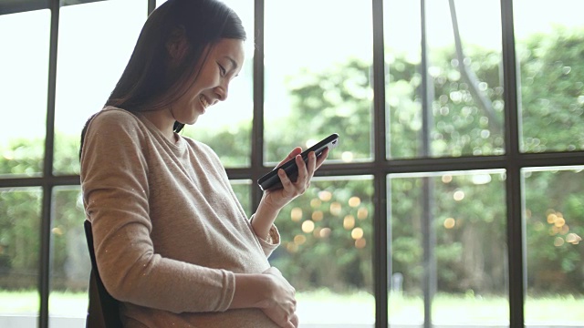 年轻孕妇在家里使用智能手机视频素材