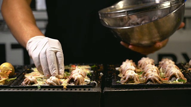 4K慢镜头特写厨师烹饪和添加章鱼配料的日式章鱼烧锅，传统风格和街头食物的概念视频素材