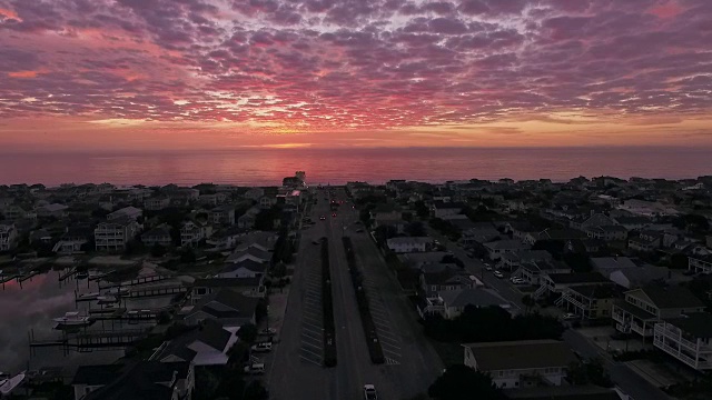 无人机豪华海滩别墅鸟瞰图在壮观的粉红色日出在Wrightsville海滩，汽车开过桥视频素材