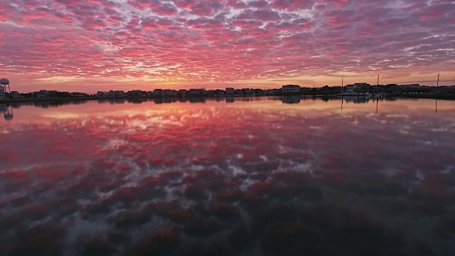 无人机在Wrightsville海滩豪华别墅前的低空鸟瞰图，壮观的粉红色日出倒映在涟漪的水面上视频素材