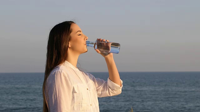 一个女人在海滩上喝瓶子里的水视频素材