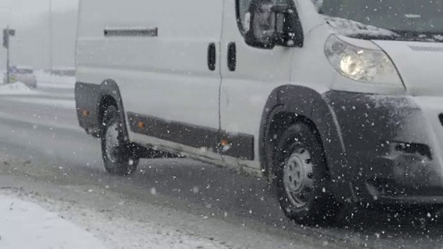 慢镜头:一场暴风雪中，白色货车沿着光滑的道路行驶。视频素材