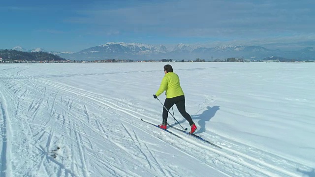 空中飞行，一个穿着彩色夹克的女人在雪道上滑雪。视频素材