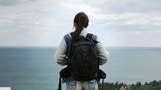 在阴雨的天气里，背包里戴着太阳镜的徒步旅行者欣赏令人惊叹的海景视频素材