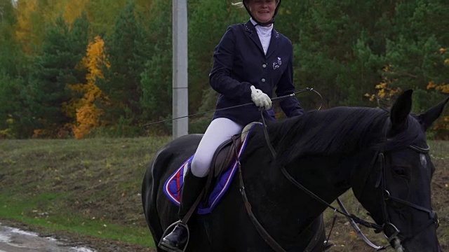 一位穿着黑白骑师服的年轻女子骑着马慢慢地骑马。休息时间马术运动比赛之间的休息时间缓慢的运动。视频素材