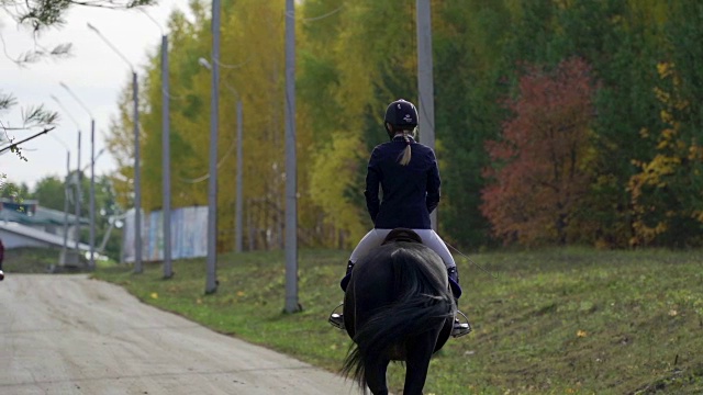 一位穿着黑白骑师服的年轻女子骑着马慢慢地骑马。休息时间马术运动比赛之间的休息时间缓慢的运动。视频素材