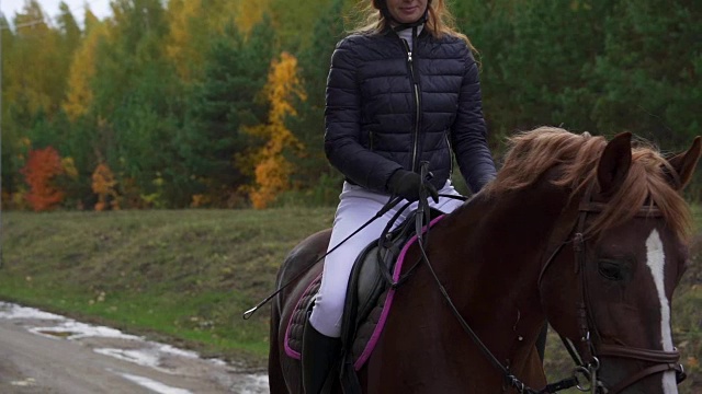 一位穿着黑白骑师服的年轻女子骑着马慢慢地骑马。休息时间马术运动比赛之间的休息时间缓慢的运动。视频素材