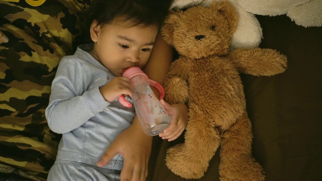亚洲女孩用奶瓶喝牛奶，抱着泰迪熊视频素材