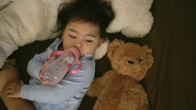 一个用奶瓶喝牛奶的亚洲女孩。持有的泰迪熊视频素材
