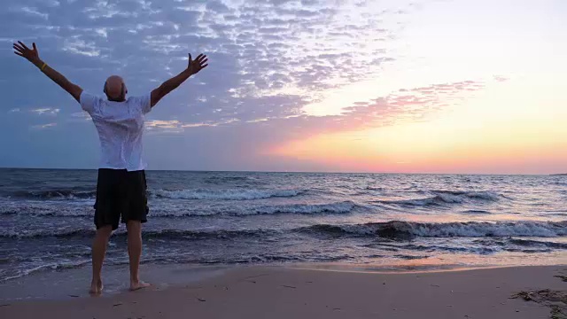 日出时，海面上的自由人在海滩上举起双手视频素材