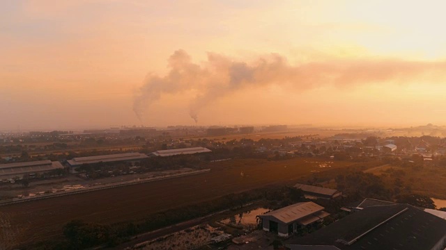 一架无人机在清晨冬日日落时分用烟雾射向农村工厂的管道。视频素材