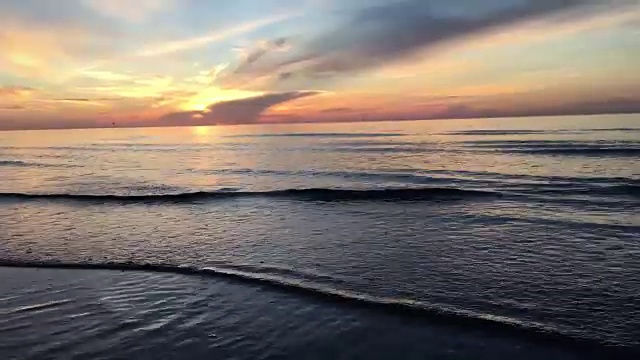 海滩上的日落-宁静的田园诗般的景象，一个金色的日落在海上，海浪慢慢溅在沙滩上视频素材