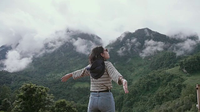 女游客探索山坡，站在山顶，欣赏周围的壮丽的山在一个美丽的阳光灿烂的日子视频素材