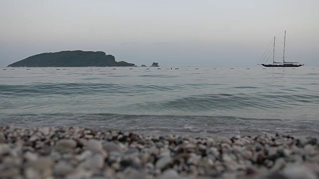 海浪拍打在多石的海滩上。背景是游艇和岛屿视频素材