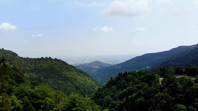 意大利比利亚奥罗帕- 2018年7月7日:航空。美丽的风景，美丽的全景的山区地形覆盖着浓密的绿色植物，森林，对着天空。这座城市在远处看得见视频素材