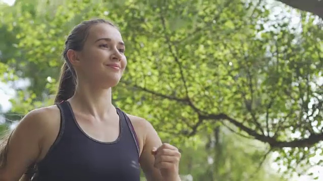 微笑的女人在阳光下跑步，早晨在新鲜的空气中慢跑，美丽的运动视频素材