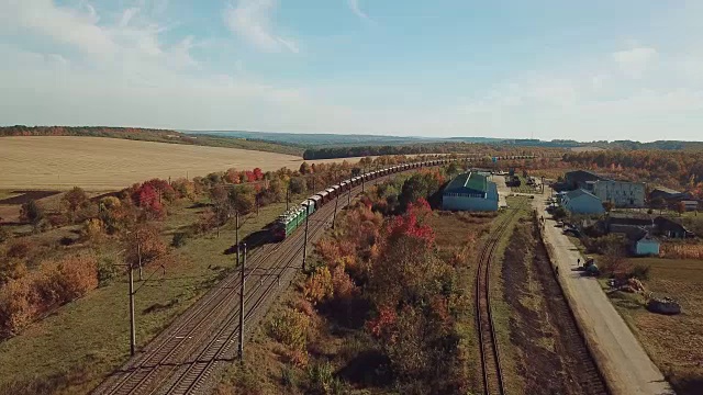 在田野和公路的乡村背景下，一列货运火车正通过铁路驶向最近的城镇。视频素材