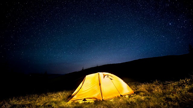 延时。在繁星点点的夜空下，在山林中闪闪发光的露营帐篷视频素材