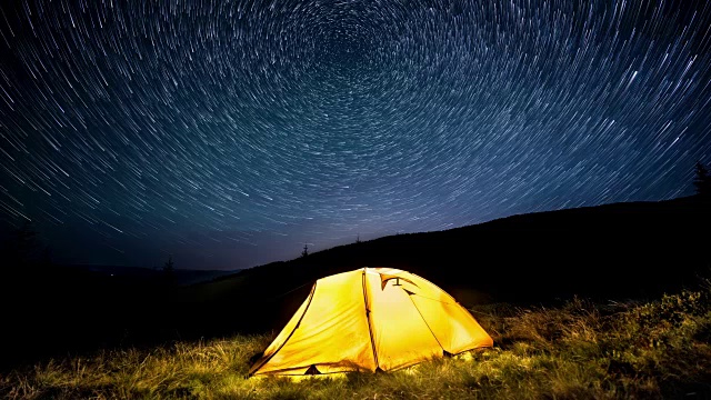 延时。星星在夜山和发光的露营帐篷上空盘旋视频素材