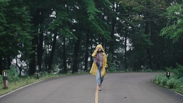 森林附近的路年轻的亚洲女人穿着黄色雨衣漫步在森林里视频素材