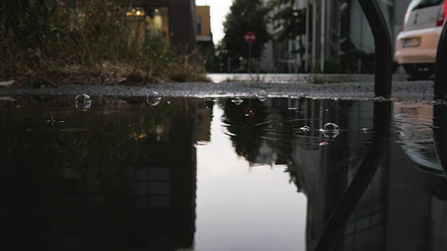 雨水在水坑中形成气泡，反射天空，建筑物和交通视频素材