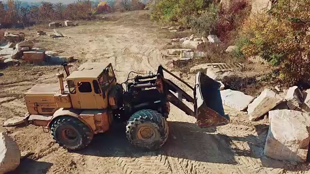 在有森林的小山附近的采石场里，有专门的采石机器和一个铲斗在工作。视频素材