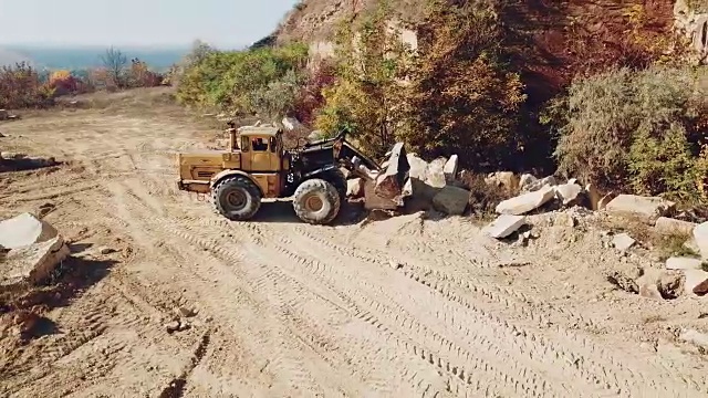 专业的黄色推土机带着一个铲斗正在采石场以石头为背景的沙子中工作。视频素材