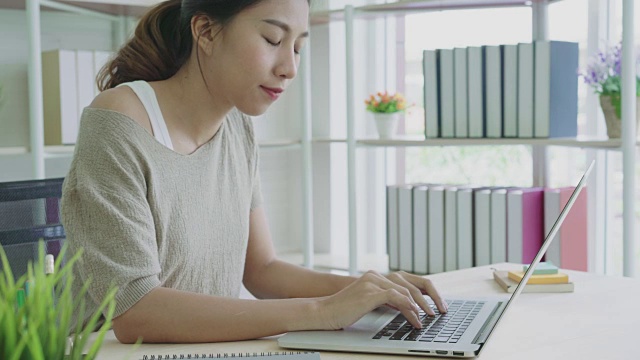 迷人的年轻亚洲女人在家里工作看着笔记本电脑感觉周到和思考创意的概念自由嬉皮士。视频素材