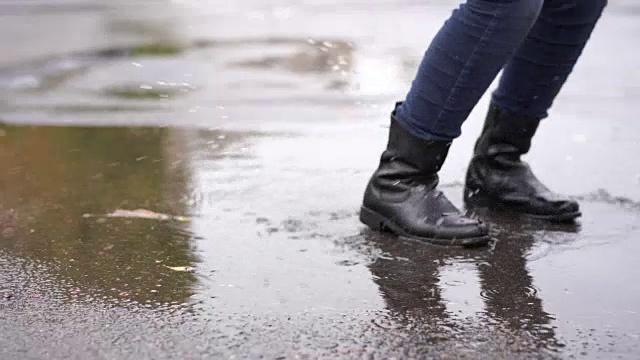 雨中，一个穿着黑色皮靴的女孩在秋天的水坑里绊了一跤视频素材