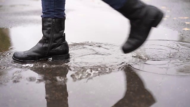 一个穿着黑色皮靴的女孩慢镜头走在秋雨中的水坑里视频素材