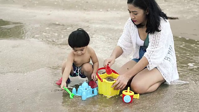 妈妈和儿子在沙滩上玩沙子玩具视频素材