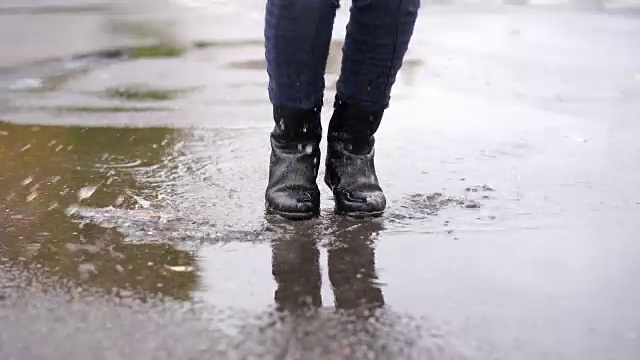 雨中，一个穿着黑色皮靴的女孩在秋天的水坑里绊了一跤视频素材