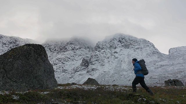 一个人背着双肩包，独自一人，在山里旅行。它沿着白雪覆盖的高峰而行。视频素材