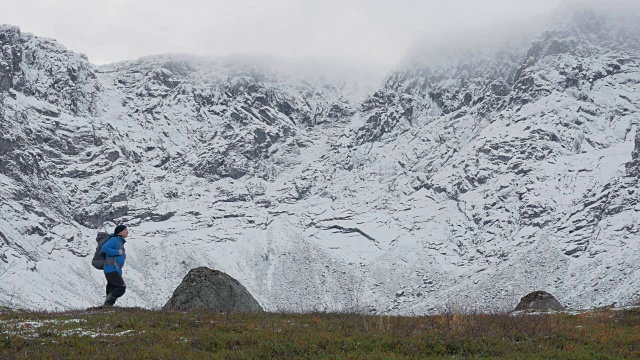 一个人背着双肩包，独自一人，在山里旅行。它沿着白雪覆盖的高峰而行。视频素材