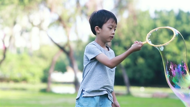 欢快的蹒跚学步的小男孩在公园里玩肥皂泡视频素材