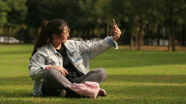 亚洲大学女孩坐在草地上使用手机在校园里视频素材