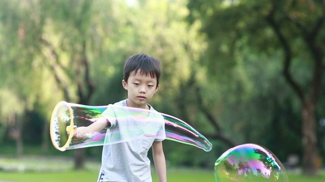 欢快的蹒跚学步的小男孩在公园里玩肥皂泡视频素材