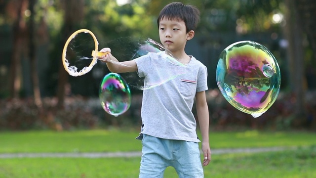 欢快的蹒跚学步的小男孩在公园里玩肥皂泡视频素材