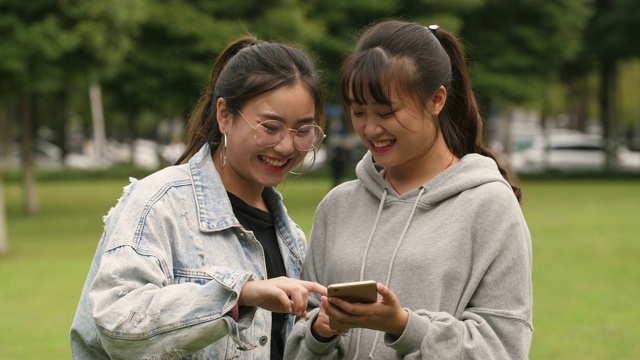 两个亚洲女大学生在校园里使用手机视频素材