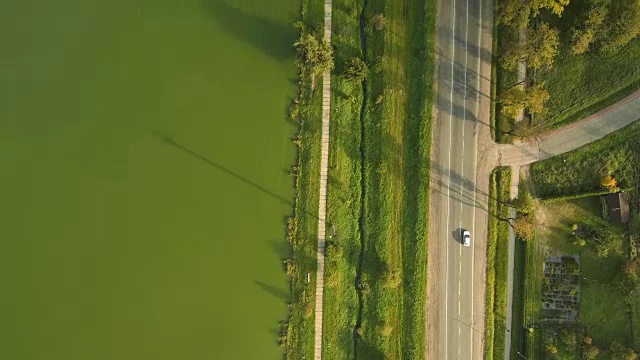 无人机鸟瞰图:道路与一辆车沿着绿色的湖。视频素材