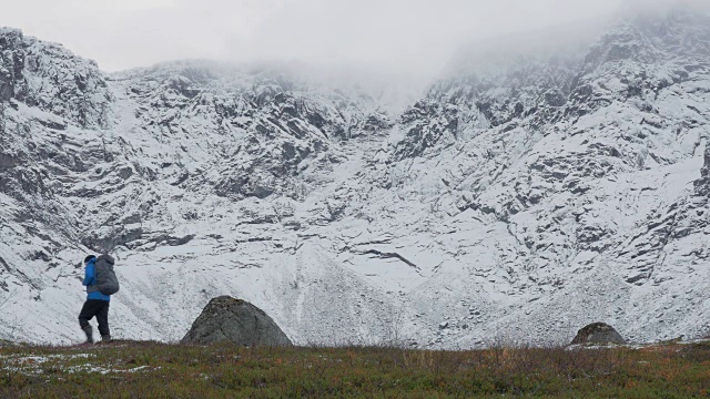 一个人背着双肩包，独自一人，在山里旅行。它沿着白雪覆盖的高峰而行。视频素材